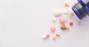 - Tennessee Behavioral Health Assorted pills and capsules spilled from a blue medicine bottle onto a pale surface.