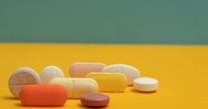 - Tennessee Behavioral Health Assorted capsules and tablets in pastel colors scattered on a bright yellow surface.