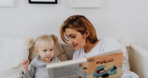 - Tennessee Behavioral Health Woman reading a children's book to a young girl on a white sofa in a cozy living room.