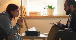 Woman with red hair speaks with a male therapist during a counseling session in a warm, well-lit office.