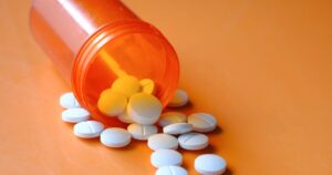 Orange prescription bottle tipped over with white round pills scattered on an orange surface.