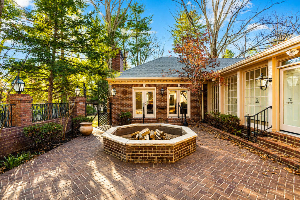 562b83d7-6b72-41b7-98ae-d4fee4b23133 - Tennessee Behavioral Health Brick-paved courtyard with a circular stone fire pit at the center, surrounding planters and a brick house with glass doors and white trim.