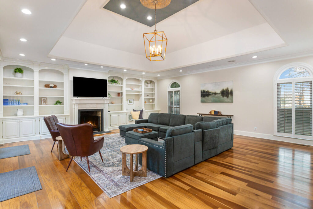 tbh-addiction-treatment-center-living-room3 - Tennessee Behavioral Health Living room with white built-in shelves, a fireplace, wall-mounted TV, and a dark blue sectional on wooden floors.