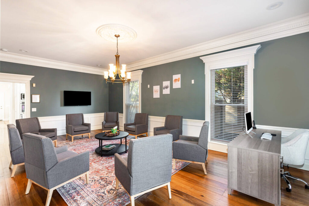 tbh-addiction-treatment-center-living-room4 - Tennessee Behavioral Health Modern meeting room with gray armchairs arranged in a circle around a central coffee table and a chandelier above.