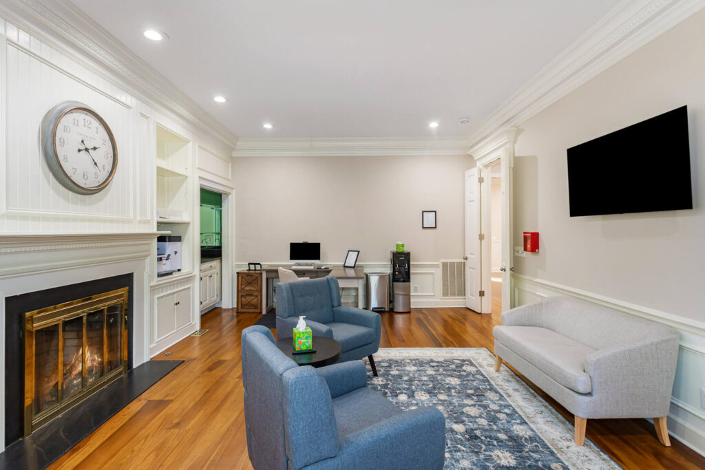 tbh-addiction-treatment-center-living-room7 - Tennessee Behavioral Health Cozy living room with white built-in shelves, a large round clock above the fireplace, and a blue upholstered seating area.