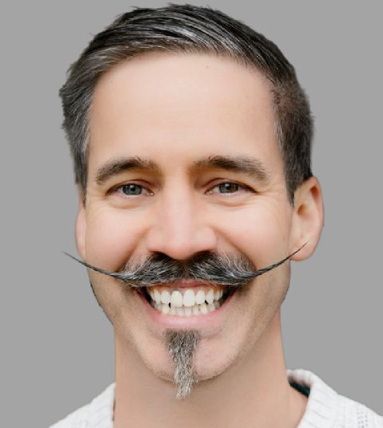 Close-up portrait of a smiling man with a styled handlebar mustache and goatee against a gray background